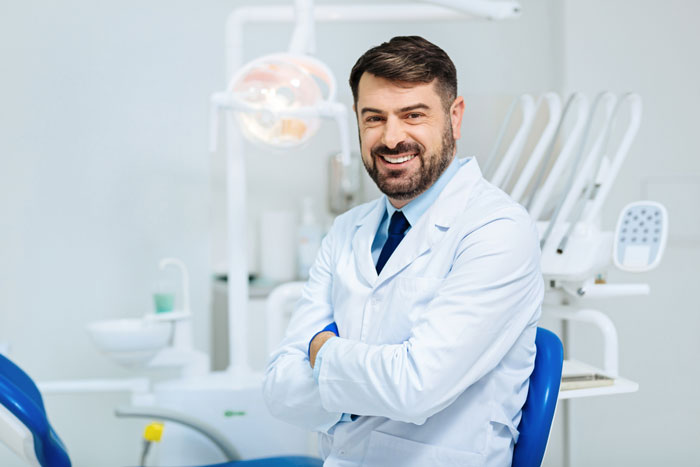 dentist smiling with arms crossed in front of dental equipment